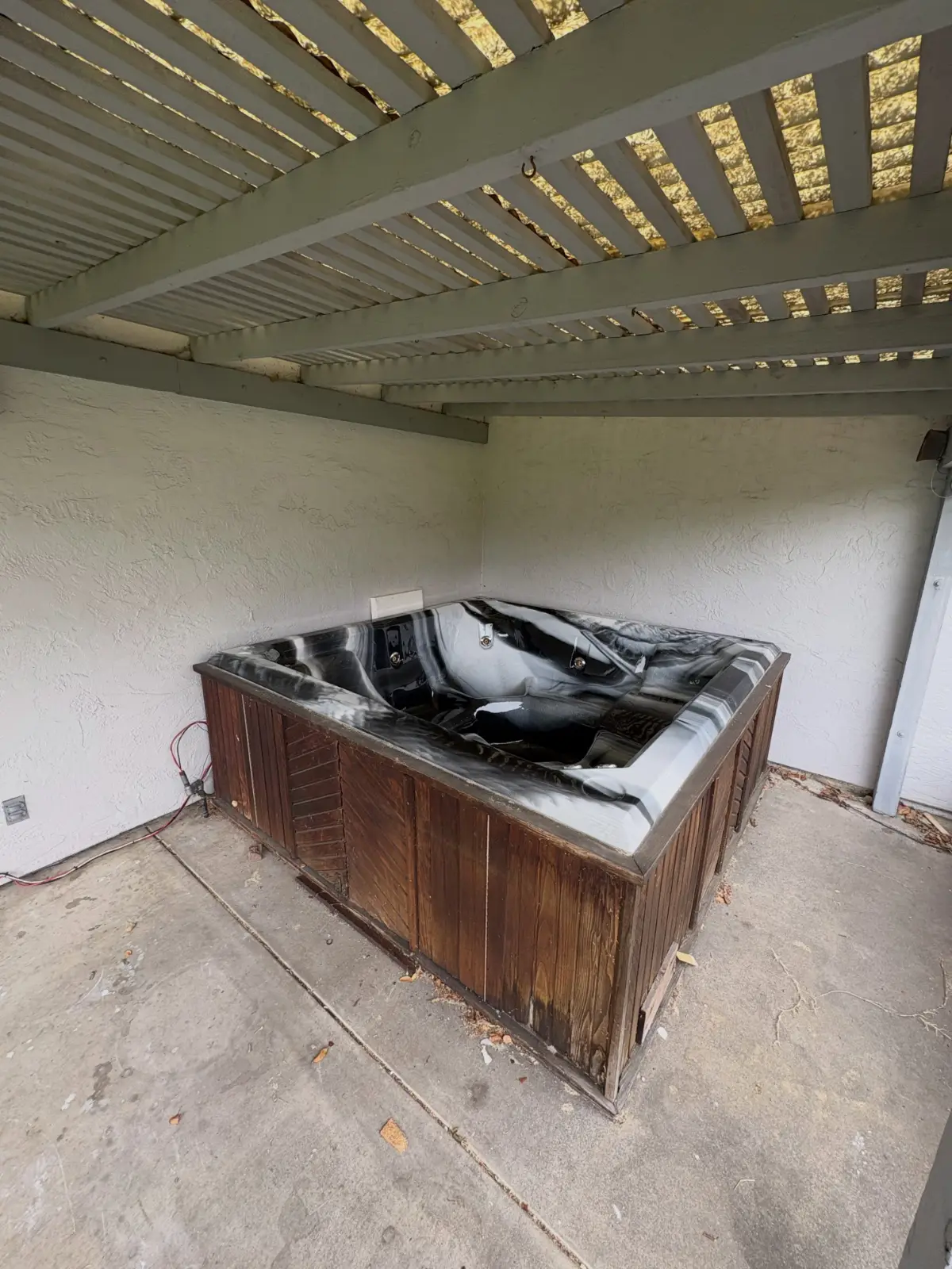 A black-marble acrylic hot tub with a dark wood skirt under a pergola at a Tempe home